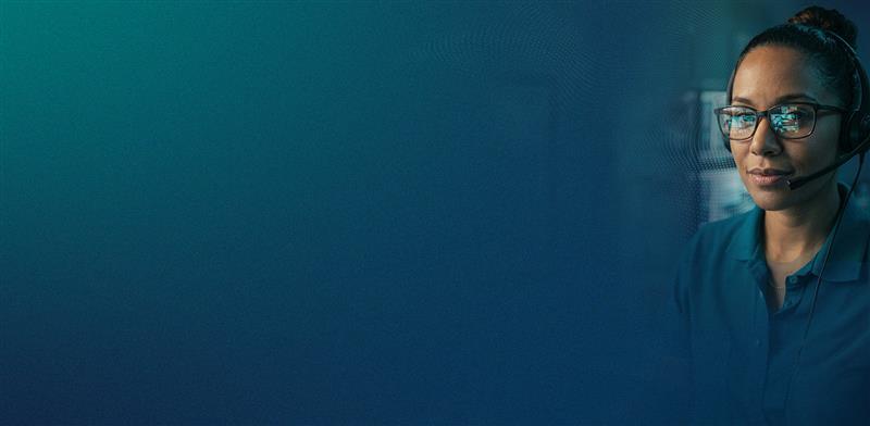 woman wearing a headshot working at a computer at a command center with data reflecting in her glasses